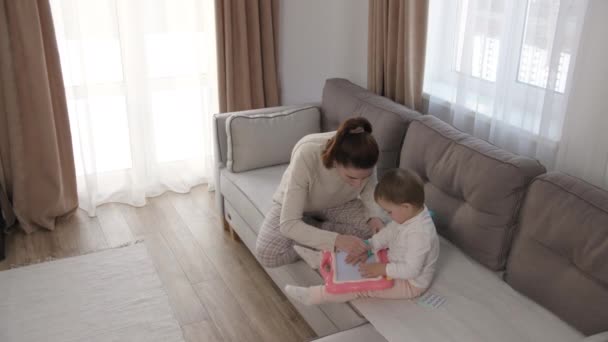 Догляд за молодою матір'ю або нянею допомагає своїй милій доньці навчити дитину, намалювати картину олівцями, лежачи на дивані у вітальні, навчитися творчості вдома — стокове відео