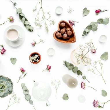 Gül tomurcuklu çalışma alanı, okaliptüs, sulu çay, bir fincan kakao, beyaz arka planda tatlılar. Düz konum, genel manzara, ev ofis çalışma alanı