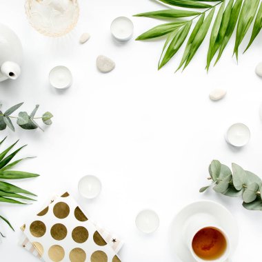 Masa çalışma alanı sulu, palmiye yaprağı dalları, çay, günlük, bardaklar ve beyaz arka planda altın tokalar. düz yatış, üst görünüm