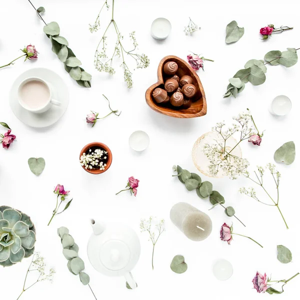 Gül tomurcuklu çalışma alanı, okaliptüs, sulu çay, bir fincan kakao, beyaz arka planda tatlılar. Düz konum, genel manzara, ev ofis çalışma alanı