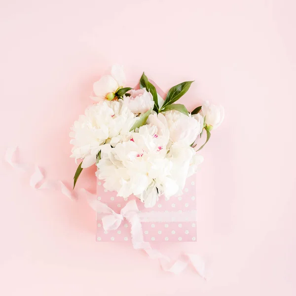 Beige bouquet of peonies in an envelope for flowers on pink background. Minimal floral concept greeting card. Flat lay, top view.