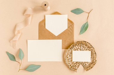 Sahte düğün davetiyesi, boş tebrik kartı ve el işi zarfı, yeşil yapraklı okaliptüs. Düz yatış, üst görünüm.