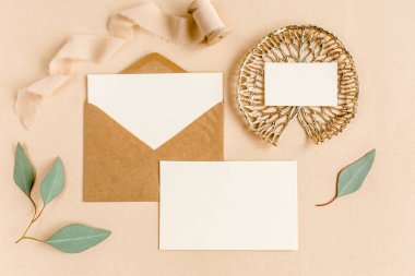 Sahte düğün davetiyesi, boş tebrik kartı ve el işi zarfı, yeşil yapraklı okaliptüs. Düz yatış, üst görünüm.