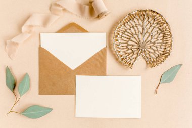 Sahte düğün davetiyesi, boş tebrik kartı ve el işi zarfı, yeşil yapraklı okaliptüs. Düz yatış, üst görünüm.