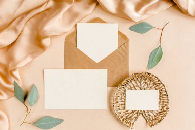 Sahte düğün davetiyesi, boş tebrik kartı ve el işi zarfı, yeşil yapraklı okaliptüs. Düz yatış, üst görünüm.