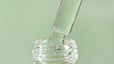 Gri zemin üzerinde yağ damlaları olan kozmetik pipeti