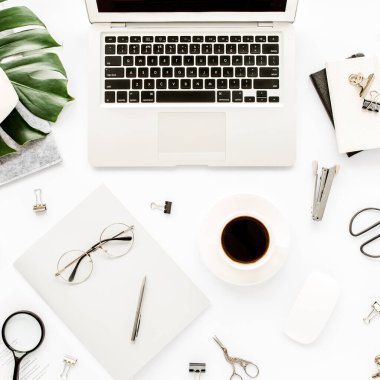 Ev ofisinin çalışma alanı dizüstü bilgisayarı, tropikal yaprakları Monstera, not panosu, defter ve aksesuarları beyaz arka planda. Düz yatış, üst görünüm