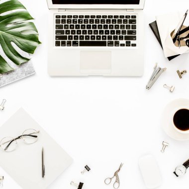 Ev ofisinin çalışma alanı dizüstü bilgisayarı, tropikal yaprakları Monstera, not panosu, defter ve aksesuarları beyaz arka planda. Düz yatış, üst görünüm