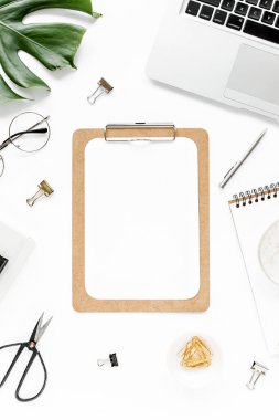 Ev ofisinin çalışma alanı dizüstü bilgisayarı, tropikal yaprakları Monstera, not panosu, defter ve aksesuarları beyaz arka planda. Düz yatış, üst görünüm