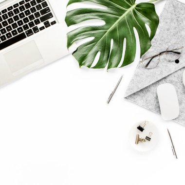 Ev ofisinin çalışma alanı dizüstü bilgisayarı, tropikal yaprakları Monstera, not panosu, defter ve aksesuarları beyaz arka planda. Düz yatış, üst görünüm