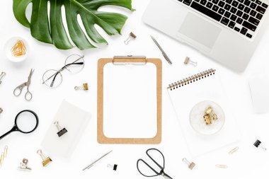 Ev ofisinin çalışma alanı dizüstü bilgisayarı, tropikal yaprakları Monstera, not panosu, defter ve aksesuarları beyaz arka planda. Düz yatış, üst görünüm