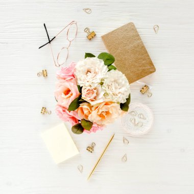 Düz uzanmış kadınların ofis masası. Pembe güller, çiçek buketi, aksesuarlar, altın günlük, beyaz ahşap arka planda gözlük.