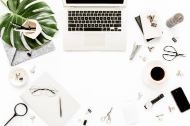 Ev ofisinin çalışma alanı dizüstü bilgisayarı, tropikal yaprakları Monstera, not panosu, defter ve aksesuarları beyaz arka planda. Düz yatış, üst görünüm