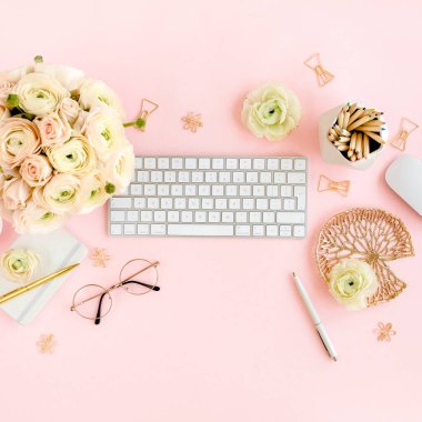 Tarz sahibi, pembe kadınların ofis masası. Bilgisayarlı çalışma alanı, buket ranunculus ve güller, pembe arka planda pano. Düz yatıyordu. Üst görünüm.