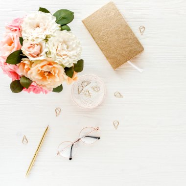 Düz uzanmış kadınların ofis masası. Pembe güller, çiçek buketi, aksesuarlar, altın günlük, beyaz ahşap arka planda gözlük.