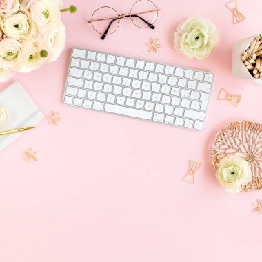 Tarz sahibi, pembe kadınların ofis masası. Bilgisayarlı çalışma alanı, buket ranunculus ve güller, pembe arka planda pano. Düz yatıyordu. Üst görünüm.