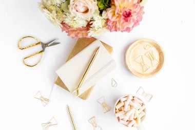 Ev ofisinin masası düzdü. Pembe güllü kadın çalışma alanı, yıldız çiçeği buketi, altın aksesuarlar, beyaz arka planda günlük. Üst görünüm.