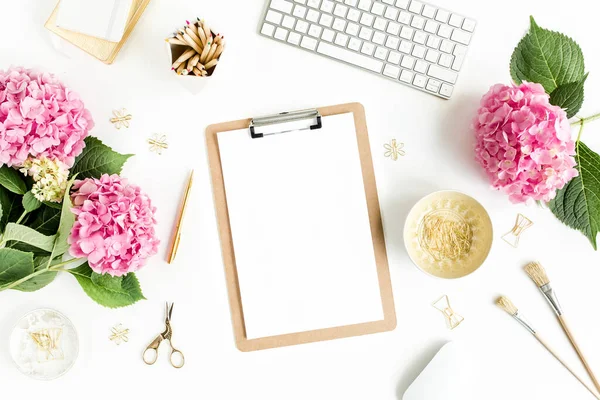 Meja wanita yang bergaya. Ruang kerja dengan papan klip, komputer, bouquet hydrangea, aksesoris pada latar belakang putih. Berbaringlah. Tampilan atas. — Stok Foto