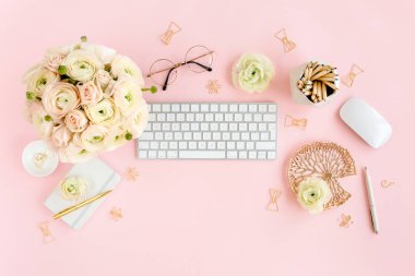 Tarz sahibi, pembe kadınların ofis masası. Bilgisayarlı çalışma alanı, buket ranunculus ve güller, pembe arka planda pano. Düz yatıyordu. Üst görünüm.