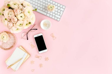Tarz sahibi, pembe kadınların ofis masası. Bilgisayarlı çalışma alanı, buket ranunculus ve güller, pembe arka planda telefon. Düz yatıyordu. Üst görünüm.