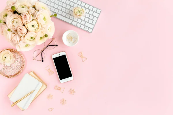 Tarz sahibi, pembe kadınların ofis masası. Bilgisayarlı çalışma alanı, buket ranunculus ve güller, pembe arka planda telefon. Düz yatıyordu. Üst görünüm.