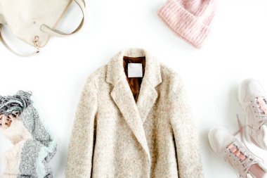 Kadın kıyafetleri ve aksesuarlar. Düz sonbahar tarzı, beyaz arka planda kalın palto, kep, spor ayakkabı giymiş bir kadın yatıyordu. Üst görünüm.