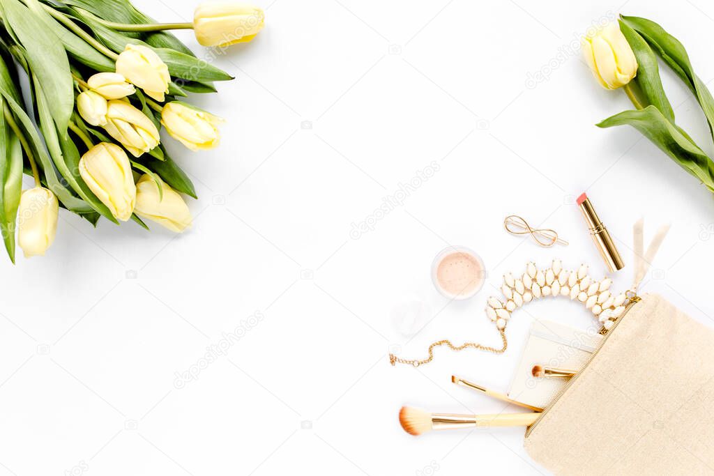 Yellow tulip flowers. Beige cosmetic bag, makeup brushes, cosmetics, golden accessories on white background. Flat composition. Top view. Flat lay. 