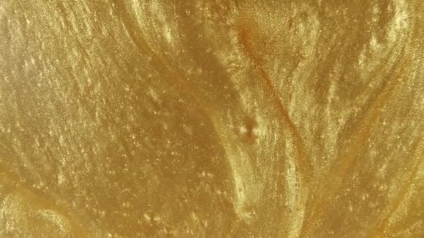 Fondo metálico líquido de oro, textura. Superposición de flujo de pintura líquida amarilla brillante primer plano. Movimiento, rotación del producto cosmético. Movimiento lento — Vídeos de Stock