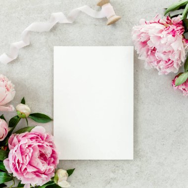 Sahte davetiye, boş kağıt tebrik kartı ve gri taş masadaki şakayıklar. Çiçek arkaplanı. Düz yatış, üst görünüm.