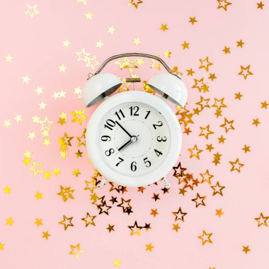 Alarmlı saat, altın yıldızlı konfeti kaplıydı. Pembe, şenlikli bir arka planda süsleme vardı. Noel ya da yeni yıl şablonu. Renkli bir kutlama, doğum günü.