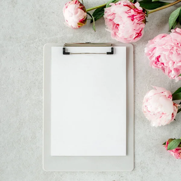Sahte davetiye, boş kağıt tebrik kartı ve gri taş masadaki şakayıklar. Çiçek arkaplanı. Düz yatış, üst görünüm.