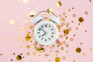 Alarmlı saat, altın yıldızlı konfeti kaplıydı. Pembe, şenlikli bir arka planda süsleme vardı. Noel ya da yeni yıl şablonu. Renkli bir kutlama, doğum günü.