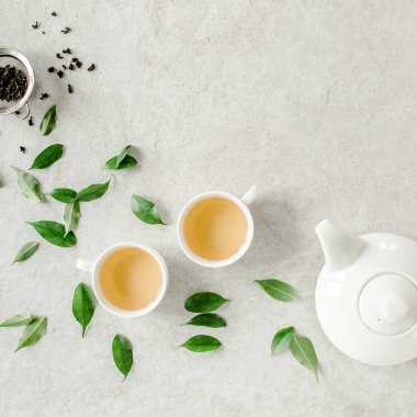 İki beyaz çay fincanı ve yeşil çay yapraklı çaydanlık ile bitki çayı. Düz yerde, üst tarafta. Çay konsepti