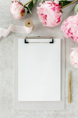 Sahte davetiye, boş kağıt tebrik kartı ve gri taş masadaki şakayıklar. Çiçek arkaplanı. Düz yatış, üst görünüm.