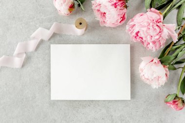 Sahte davetiye, boş kağıt tebrik kartı ve gri taş masadaki şakayıklar. Çiçek arkaplanı. Düz yatış, üst görünüm.