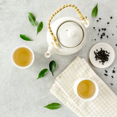 İki beyaz çay fincanı ve yeşil çay yapraklı çaydanlık ile bitki çayı. Düz yerde, üst tarafta. Çay konsepti