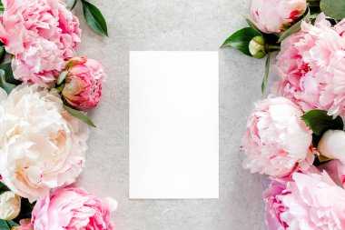 Sahte davetiye, boş kağıt tebrik kartı ve gri taş masadaki şakayıklar. Çiçek arkaplanı. Düz yatış, üst görünüm.