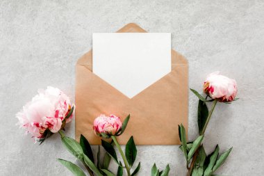 Sahte davetiye, boş kağıt tebrik kartı ve gri taş masadaki şakayıklar. Çiçek arkaplanı. Düz yatış, üst görünüm.