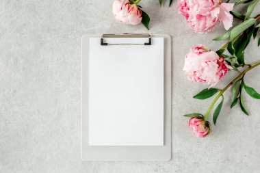 Sahte davetiye, boş kağıt tebrik kartı ve gri taş masadaki şakayıklar. Çiçek arkaplanı. Düz yatış, üst görünüm.