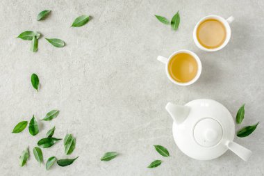 İki beyaz çay fincanı ve yeşil çay yapraklı çaydanlık ile bitki çayı. Düz yerde, üst tarafta. Çay konsepti