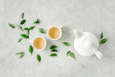 İki beyaz çay fincanı ve yeşil çay yapraklı çaydanlık ile bitki çayı. Düz yerde, üst tarafta. Çay konsepti