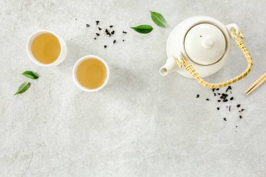 İki beyaz çay fincanı ve yeşil çay yapraklı çaydanlık ile bitki çayı. Düz yerde, üst tarafta. Çay konsepti