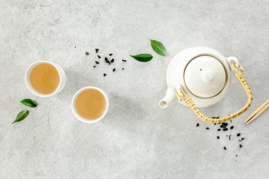 İki beyaz çay fincanı ve yeşil çay yapraklı çaydanlık ile bitki çayı. Düz yerde, üst tarafta. Çay konsepti