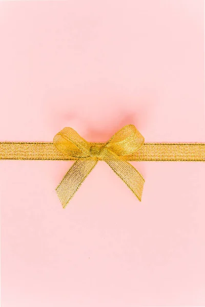 Zlatá stuha s lukem, izolovaná na růžovém pozadí. Barevná oslava, narozeninové pozadí. Byt ležel, horní pohled — Stock fotografie