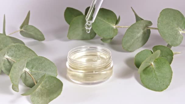 Pipetta con olio di eucalipto con foglie su fondo bianco. Estratto di eucalipto, olio essenziale aromatico. Cosmetici naturali per capelli e cura della pelle. Vista dall'alto. — Video Stock