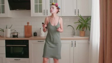 Aktif genç bir kadın dans ediyor, uzaktan kumandaya şarkı söylüyor, müzik videoları izliyor, modern bir mutfakta müzik dinliyor, evde yemek hazırlıyor, kendi başının çaresine bakıyor.