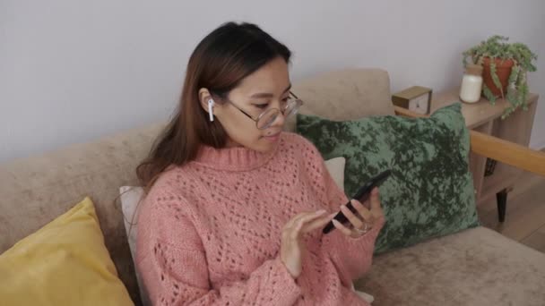 Bliskowschodnia młoda kobieta korzystająca ze smartfona surfującego po mediach społecznościowych, grająca w gry mobilne, sprawdzająca wiadomości lub SMS-y siedzące na sofie. Kobieta spędza czas w domu z technologii gadżet komórkowy. — Wideo stockowe