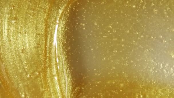 Flüssiger metallischer Goldgrund, Textur. Funkelnde gelbe Flüssigfarbstoffe überlagern Nahaufnahmen. Bewegung, Drehung des kosmetischen Produkts. Zeitlupe — Stockvideo