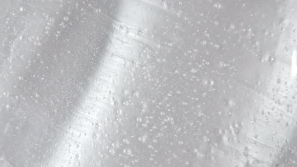 Bílé tekuté gelové pozadí, čistá sérová textura. Pohyb, otočení vzorku kosmetického výrobku s bublinkami. Horní pohled. Makro snímek — Stock video