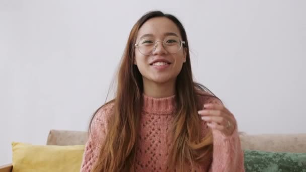 ヘッドフォンの美しいアジアの若い女性は、ラップトップを使用してビデオチャットで話をし、距離を作るオンラインビデオ会議コール。女性は携帯電話のガジェット技術で家で時間を過ごす — ストック動画